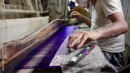 Old experienced Indian artisan hand weaving a Banarasi silk saree on a traditional wooden handloom. Adding thread to the weft shuttle