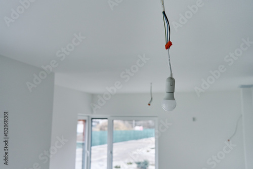 Obraz na płótnie Single light bulb hanging from exposed electrical wires in unfinished interior with white walls and concrete flooring. Lighting in building under renovation w salonie