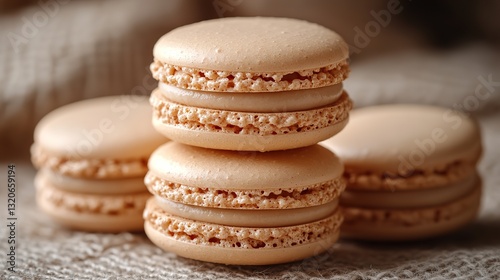 Four beige macarons, stacked on a textured beige surface, create a visually appealing arrangement against a complementary beige background.