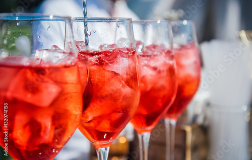 A wine glass filled with ice cubes with red wine, pink vermouth, and a red drink. Cocktail preparation at a party, Iced wine, selective focus. Refreshing cocktail in summer. Beach bar, cold drinks