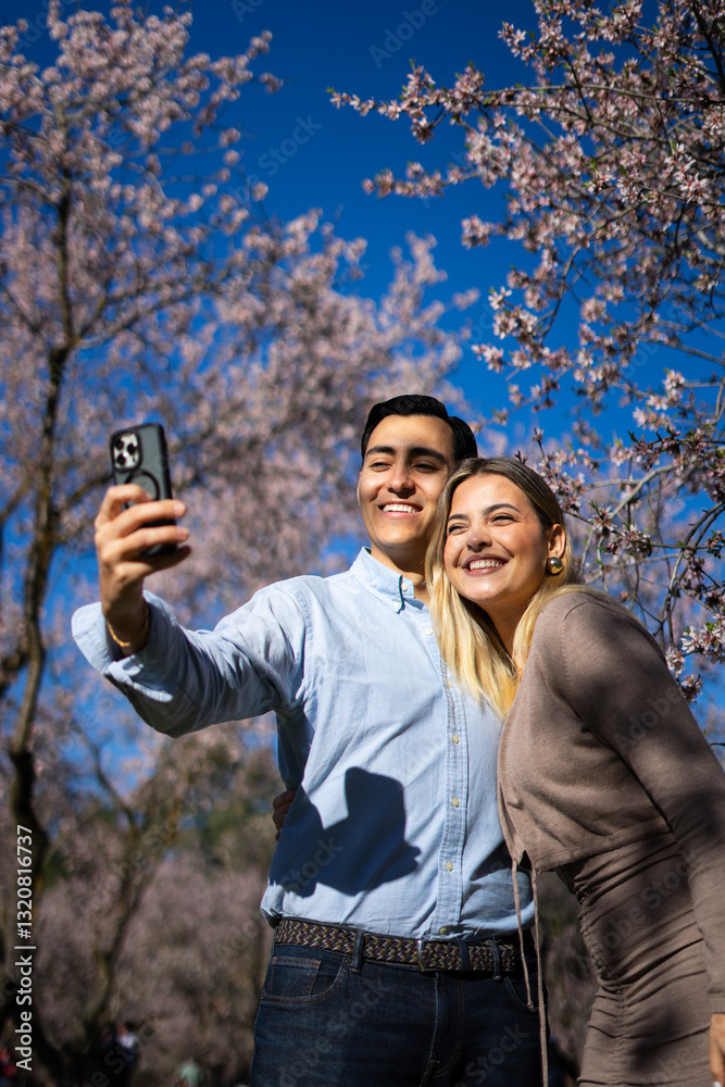 Happy latin couple taking a selfie under blooming almond trees Happy latin couple taking a selfie under blooming almond trees