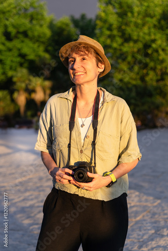 Female photographer smiling and holding camera in a public event at sunset