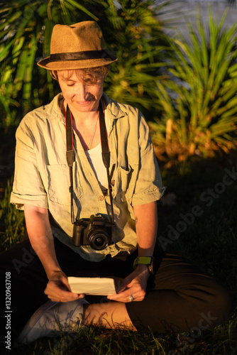 Photographer smiling and looking at printed photo while sitting on grass in park