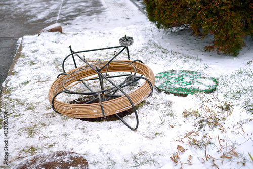 Obraz na płótnie Fiber optic cable reel placed near an open maintenance hole during broadband network installation on snowy day in telecommunications engineering site. Coiled cable on metal frame. Selective focus w salonie