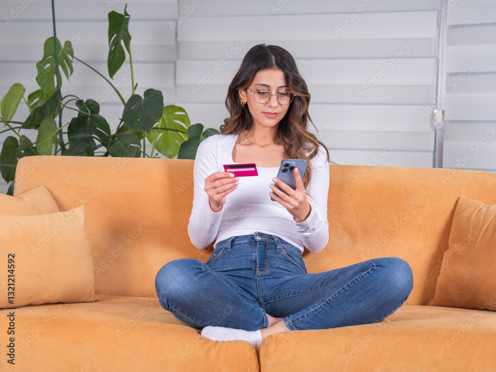 Φωτογραφία Holding credit card and mobile phone, full body view young caucasian brunette woman sit on sofa at home wear casual clothes holding credit card and mobile phone