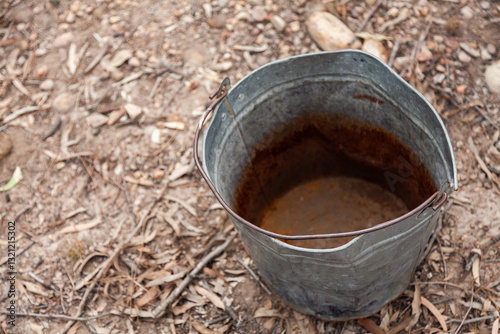 Old metal bucket on dried leaves for collecting scrap wax
