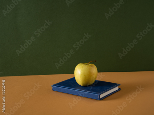 A blue notebook and a healthy apple were left on the teacher's desk during school holidays.