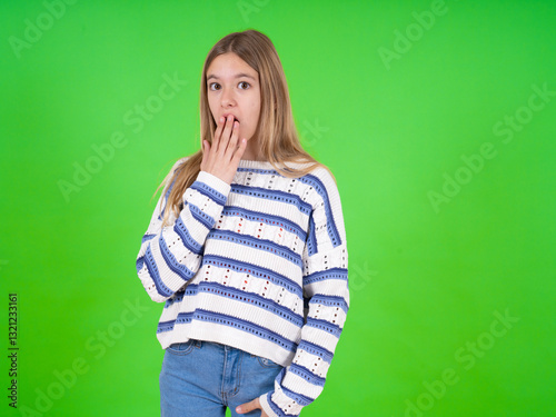 beautiful teen girl wearing striped sweater covers mouth and looks with wonder at camera, cannot believe unexpected rumors.