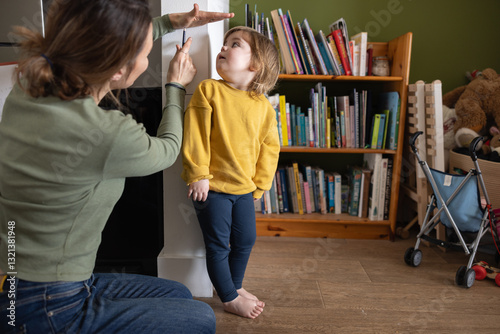 Child looking up while being measured by her mother
