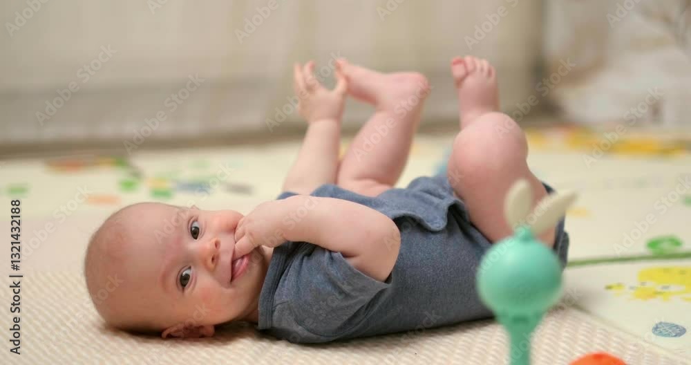 baby in blue onesie lies on play mat, grabbing its tiny feet and bringing them towards its face, infant is playful and flexible, improving coordination and mobility, playtime at home