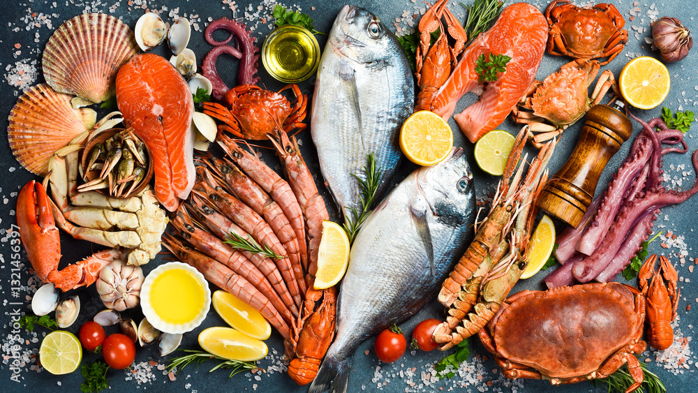Fototapeta premium Fresh Seafood Background. Assortment of seafood: Fresh fish, shrimp, oysters, lobster and octopus on slate black table. Top view.