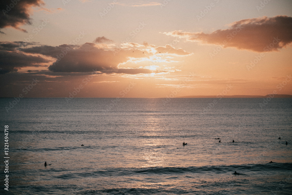 Obraz premium The sky is a beautiful orange color as the sun sets over the ocean. The water is calm and the surfers are enjoying the sunset