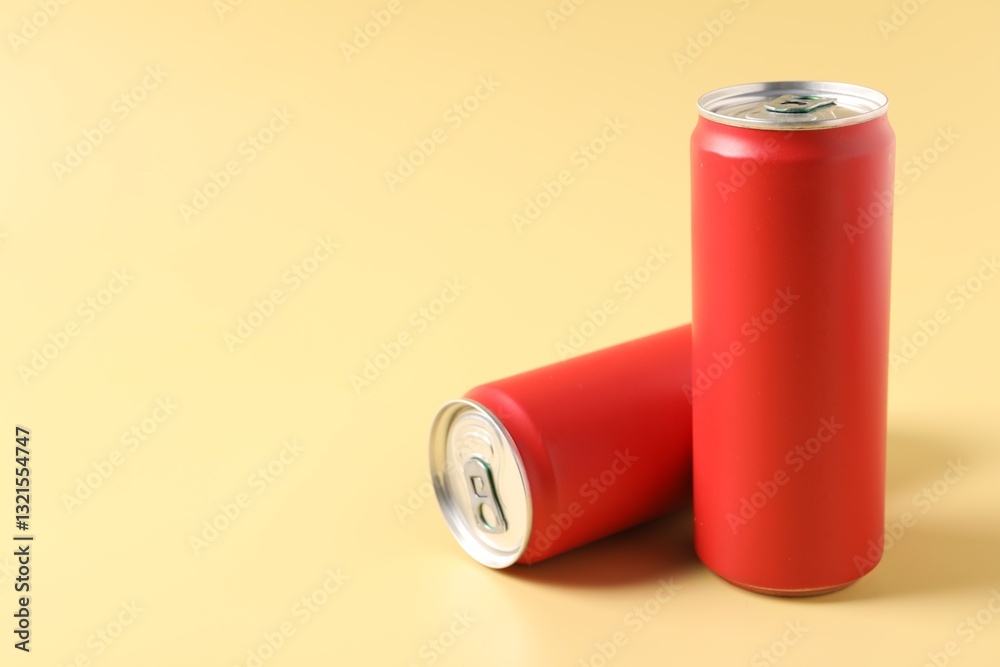 Red aluminium cans of beverage on pale yellow background, space for text Red aluminium cans of beverage on pale yellow background, space for text