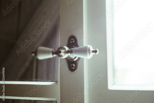 Photography Close-up of a porcelain door handle with an oblong shape, attached to a dark wood door, near a brightly lit window