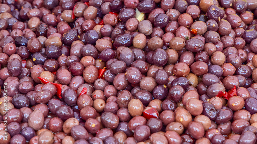 Glossy background of marinated dark olives with red chili pieces soaked in brine forming a rich textured composition Glossy background of marinated dark olives with red chili pieces soaked in brine forming a rich textured composition