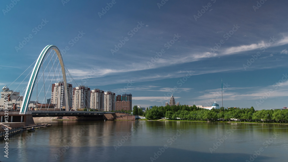 Obraz premium Bridge over Ishim with park timelapse with the transport and clouds on the background. Central Asia, Kazakhstan, Astana