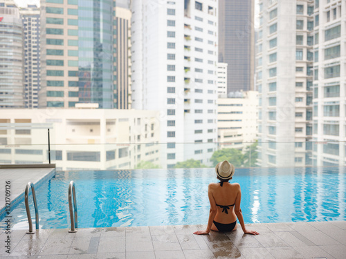 Photography Young asian woman relaxing by pool at Kuala Lumpur hotel with view of surrounding skyscrapers, enjoying leisure time in vibrant urban setting