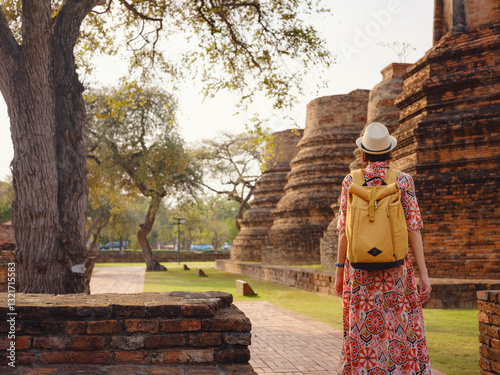 Young female tourist in dress exploring historic park of Ayutthaya, Thailand. Surrounded by ancient temples and statues, she enjoys peaceful atmosphere and rich cultural heritage.