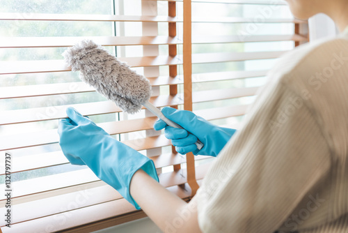 Obraz na płótnie Happy housewife asian young woman worker wearing apron and rubber gloves at home, cleaning interior working in house, use a duster to brush window blinds in living room