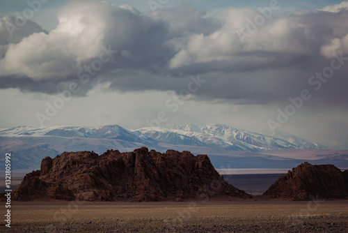 Obraz na płótnie A rugged stone landscape stretches across the foothills of western Mongolia, with snow-capped mountains looming in the background, creating a stark and dramatic scene. w salonie