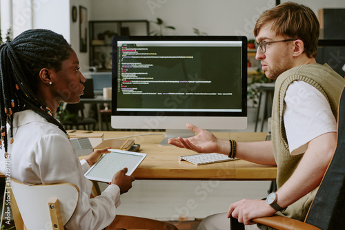 Wide shot of biracial highly qualified programmers having lively discussion in office, they sitting in modern office with digital devices photo