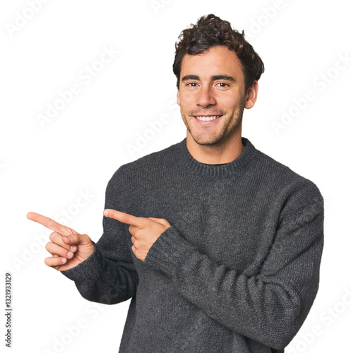 Young Hispanic man in studio excited pointing with forefingers away.