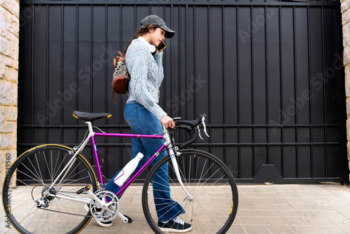 Young woman walking with her bicycle and talking on the phone