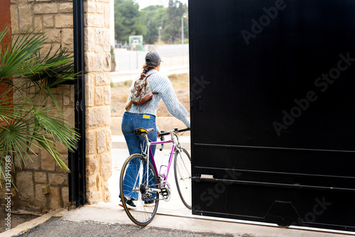 Woman opening gate while holding her bicycle entering her home