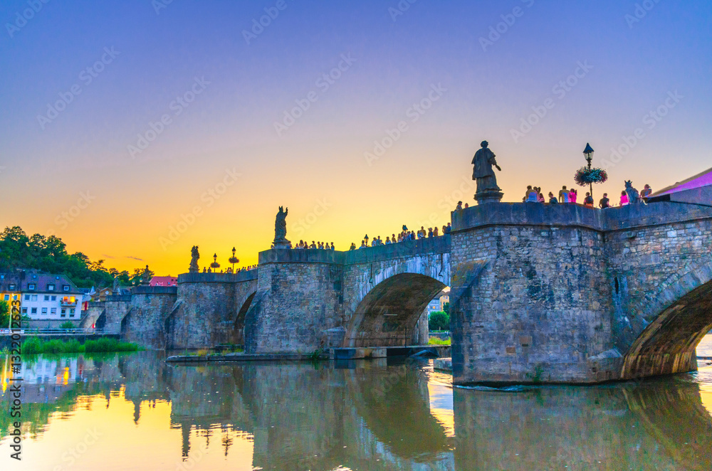 Fototapeta premium Old Main Bridge across Main river Alte Mainbrucke with statues of saints in Wurzburg old town altstadt in evening twilight dusk, Wurzburg city historical center Mitte, Bavaria state, Germany