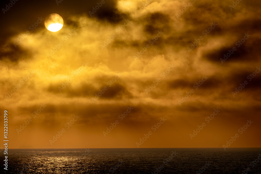 Golden skies light up the Pacific Ocean horizon with the sun revealing itself through thick coastal clouds