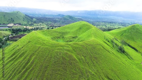 aerial view of green hills peak with grassland and mountain views of Wurung Crater, Indonesia. Aerial shot of the green grassy peak of the mountain crater.