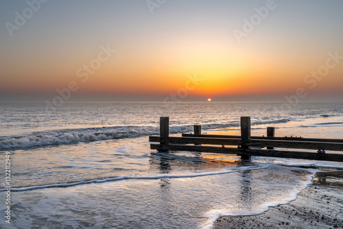 Sunrise on the beach in Mundesley, Norfolk, UK with a wooden groyne as the tide recedes photo