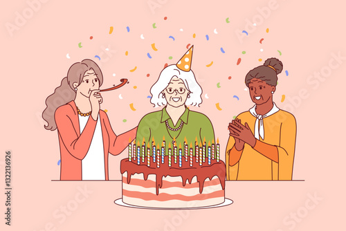 Birthday of elderly woman standing near large cake with candles and happy friends. Confetti around elderly people celebrating birthday and using whistle to create cheerful festive atmosphere