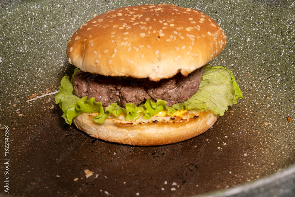A fresh sesame seed hamburger bun with beef patty, lettuce, and sauce rests on a griddle, showcasing a classic burger ready to enjoy.