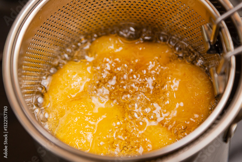 Nuggets in boiling oil in a deep fryer on a stove in a home kitchen.