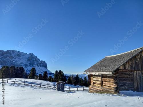 Obraz na płótnie old wooden house in the snowy mountains with a wooden fence and Alps in the background of the ski cabin with a blue sky on a sunny day in the winter w salonie