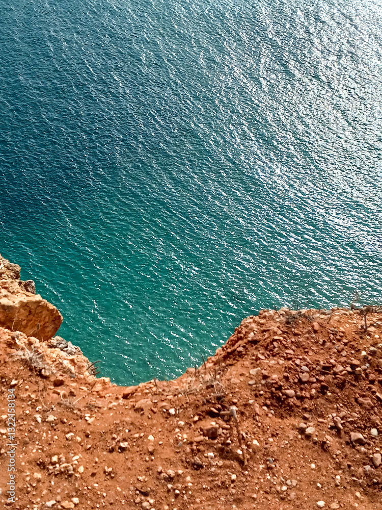 coast of the sea with orange cliffs overlooking the bright turquoise ocean by Nazare in Portugal in october. Reflection of light over the waves