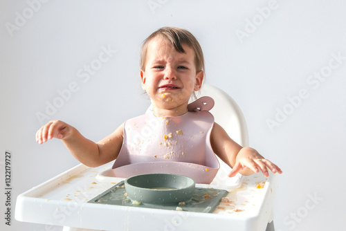 Crying toddler sitting in a high chair, covered in food, with a messy table and an upset expression, struggling during mealtime in a bright home setting