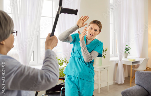 Portrait of angry elderly senior woman hitting young female nurse with crutch. Female pensioner with aggressive behavior in nursing home threatening scared medical caregiver with cane.