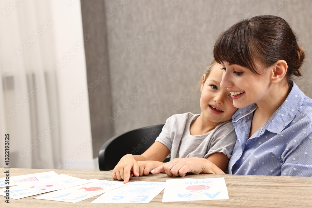 Smiling speech therapist working with little girl at table in autism treatment center. Space for text