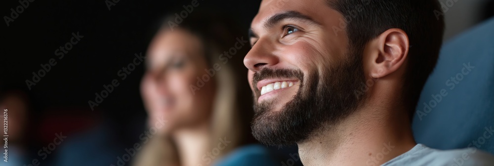 Obraz premium Capturing a moment of joy, a young man shows a bright smile while watching something engaging in a theatre, highlighting the magic of shared experiences.