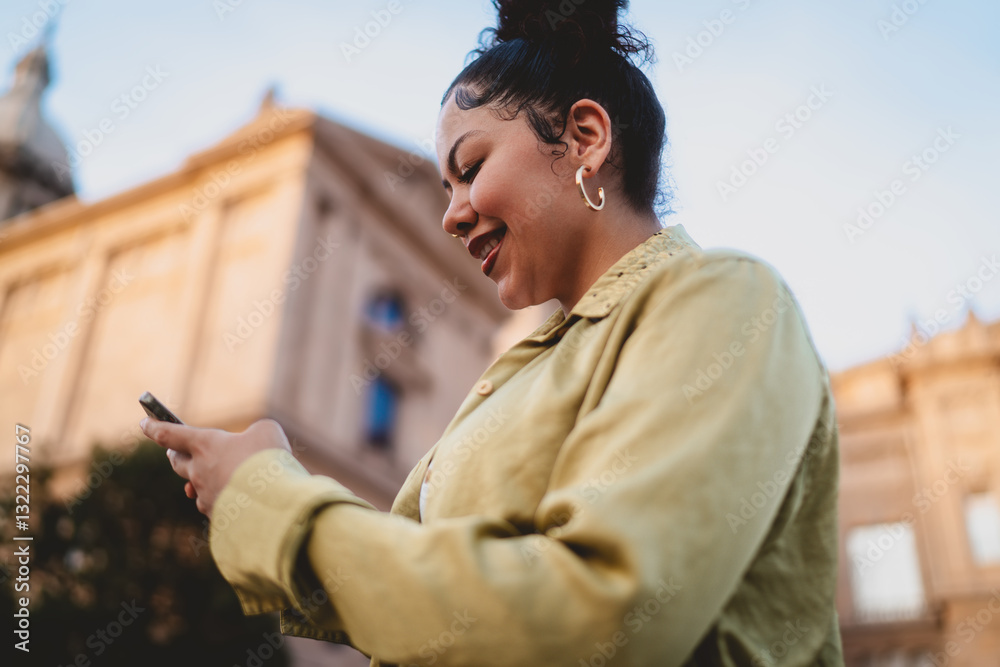 Fototapeta premium Smiling young woman using smartphone outdoors near historic building, possibly checking finances or making an online payment. image highlights mobile banking, digital economy, and financial freedom