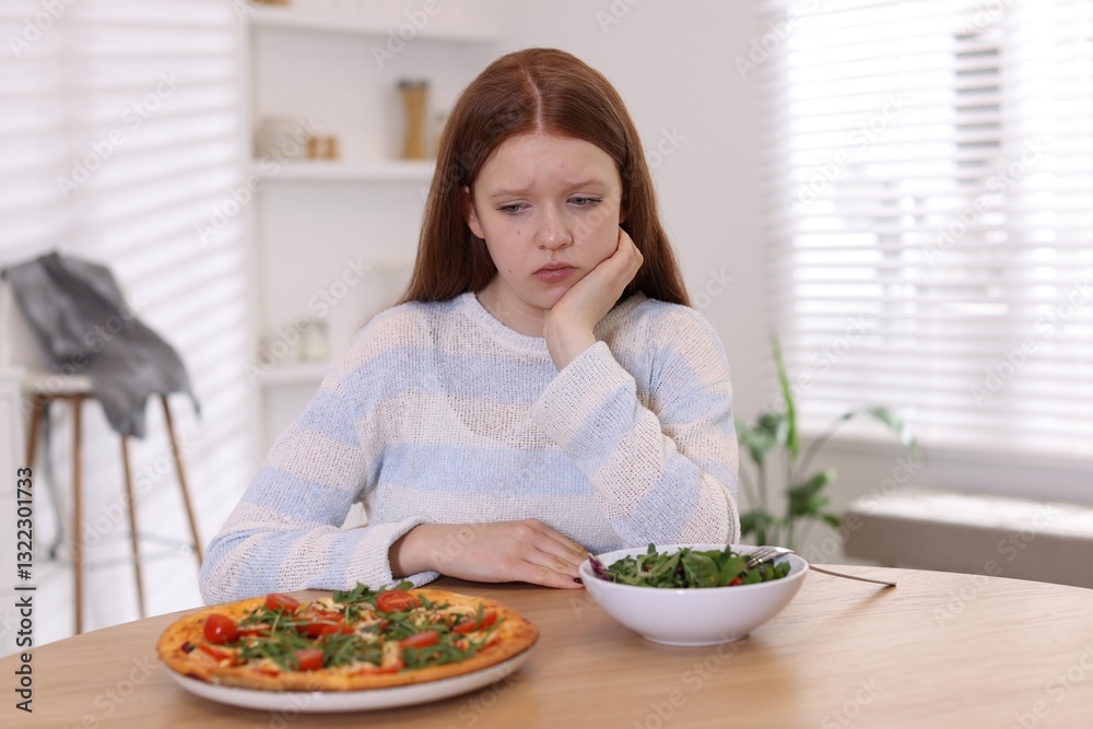 Sad teenage girl with pizza and bowl of salad at wooden table. Eating disorder Sad teenage girl with pizza and bowl of salad at wooden table. Eating disorder