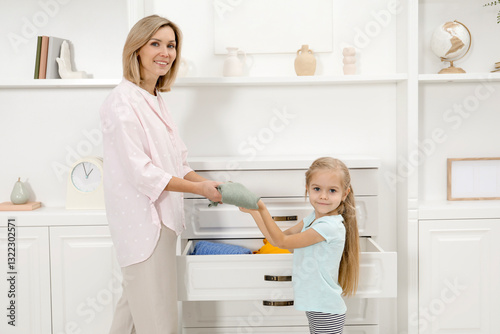 Little girl helping her mother putting clothes into drawers at home