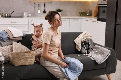Tired housewife with her little daughter among messy laundry on sofa at home