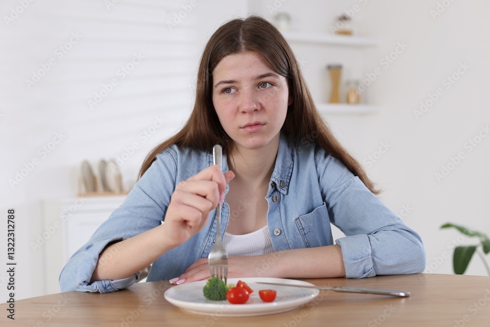 Sad teen girl holding fork with broccoli at home. Eating disorder Sad teen girl holding fork with broccoli at home. Eating disorder