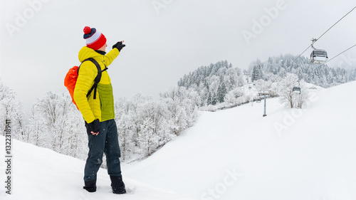 Obraz na płótnie A young man stands on the trail and shows how high the gondola lift goes. Winter landscape on a mountain hiking trail on a cloudy and foggy day. w salonie