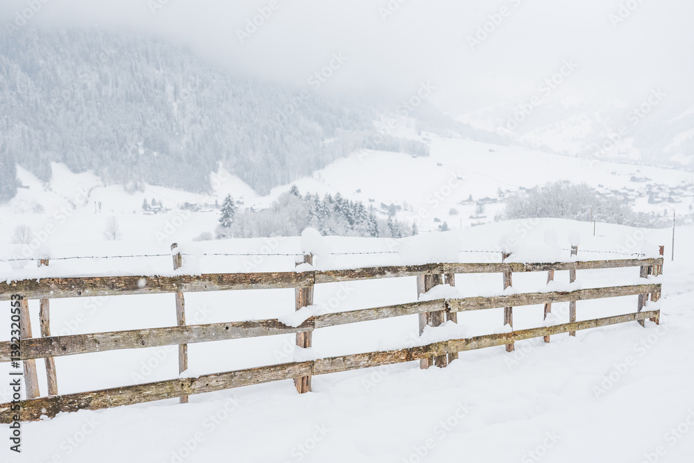Snow-covered wooden fence on a mountain pasture. Winter landscape on a mountain hiking trail on a cloudy and foggy day.