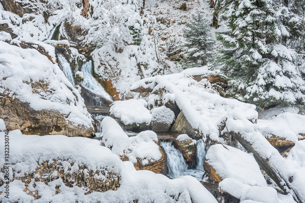 Mountain river in winter, water flows down the riverbed over snow-covered rocks. Winter landscape on a mountain hiking trail.