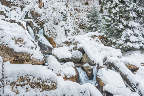 Obraz na płótnie Mountain river in winter, water flows down the riverbed over snow-covered rocks. Winter landscape on a mountain hiking trail. w salonie
